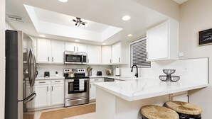 A modern kitchen with white cabinets, stainless steel appliances, and a central island with stools.