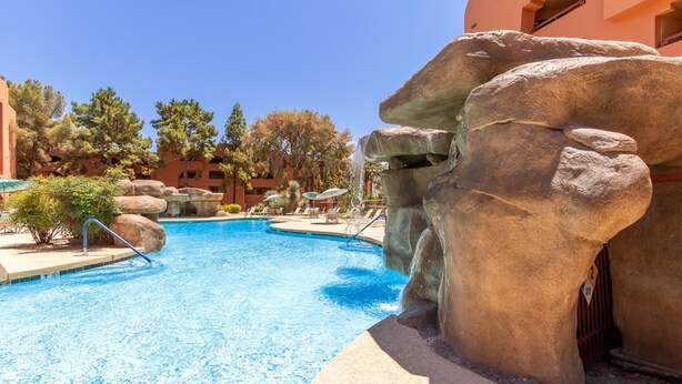 A swimming pool with a waterfall feature, surrounded by large rock formations and trees.