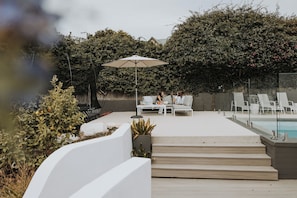 A poolside area with lounge chairs, a white umbrella, and a glass-enclosed pool.