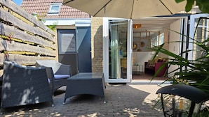 An outdoor patio with wicker furniture, a glass table, and a door leading to an interior space. - Charming and Cozy Furnished 2-person Studio Apartment (De Koog)