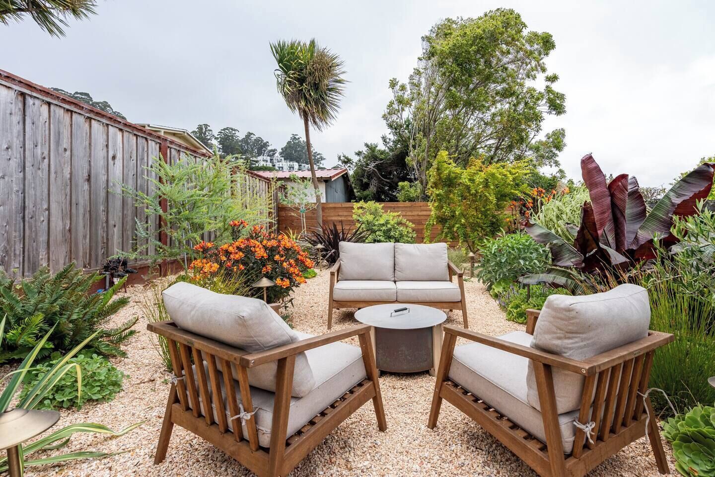 Un patio con cerramiento de madera, mobiliario exterior y una diversidad de plantas y flores.