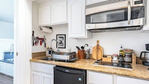 A modern kitchen with white cabinetry, a built-in microwave, a dishwasher, and a granite countertop. - Charming 1-bedroom cottage near SF (Sausalito)