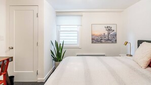 A bedroom with a bed, a window with blinds, a radiator, a plant, and a painting on the wall. - Charming 1-bedroom cottage near SF (Sausalito)