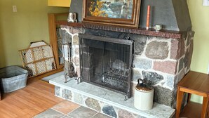 A living room with a stone fireplace, a painting above it, and a wooden floor. - Chalet Bromont ski in/ski out (Bromont)