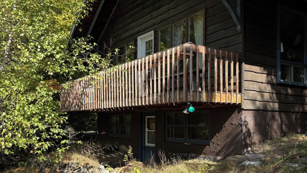 A cabin with a wooden deck, stone foundation, and a large window. - Chalet Bromont ski in/ski out (Bromont)