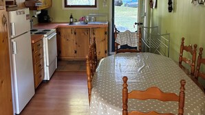A kitchen with wooden cabinets, a refrigerator, a stove, and a sink. There is a dining table with chairs and a ceiling fan. - Chalet Bromont ski in/ski out (Bromont)