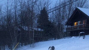 A snowy landscape with a wooden cabin and a person skiing. - Chalet Bromont ski in/ski out (Bromont)