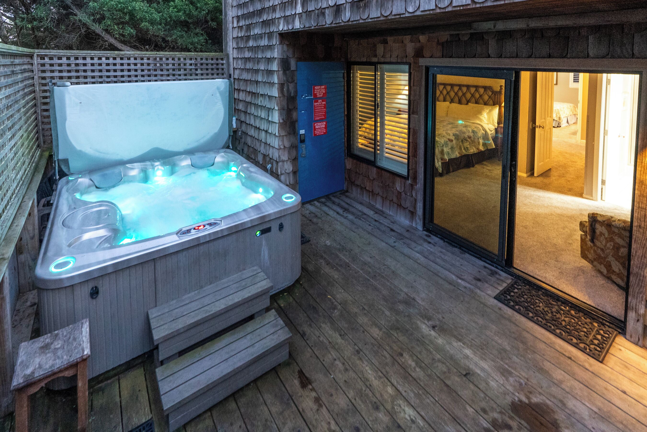 Un jacuzzi en una terraza de madera, con un dormitorio visible a través de una puerta de vidrio.