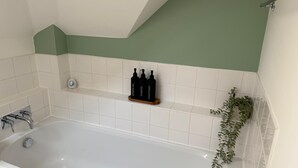 A bathroom with a white bathtub, green wall, white tiles, a shelf with black bottles, and a plant. - School Path in the heart of the historic Ironbridge (Telford)
