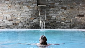 En person som simmar i en pool med en stenmur i bakgrunden.