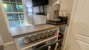 Uma cozinha com bancada de madeira, cafeteira e televisão fixada na parede.
