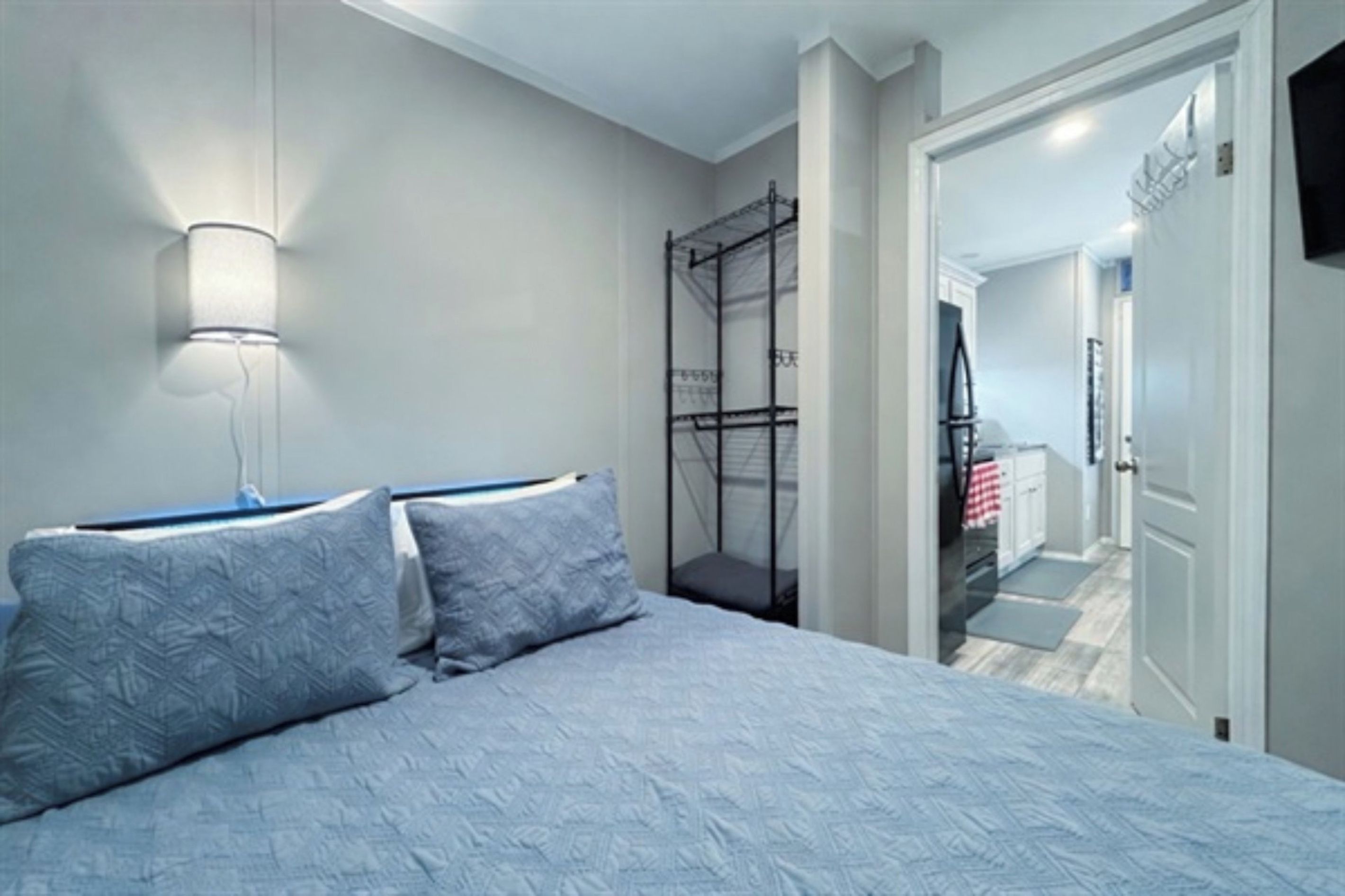 A bedroom with a bed, pillows, a nightstand, a wall-mounted lamp, and a window.