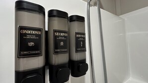 A bathroom with three dispensers labeled 'CONDITIONER,' 'SHAMPOO,' and 'BODY WASH' for daily cleaning use.
