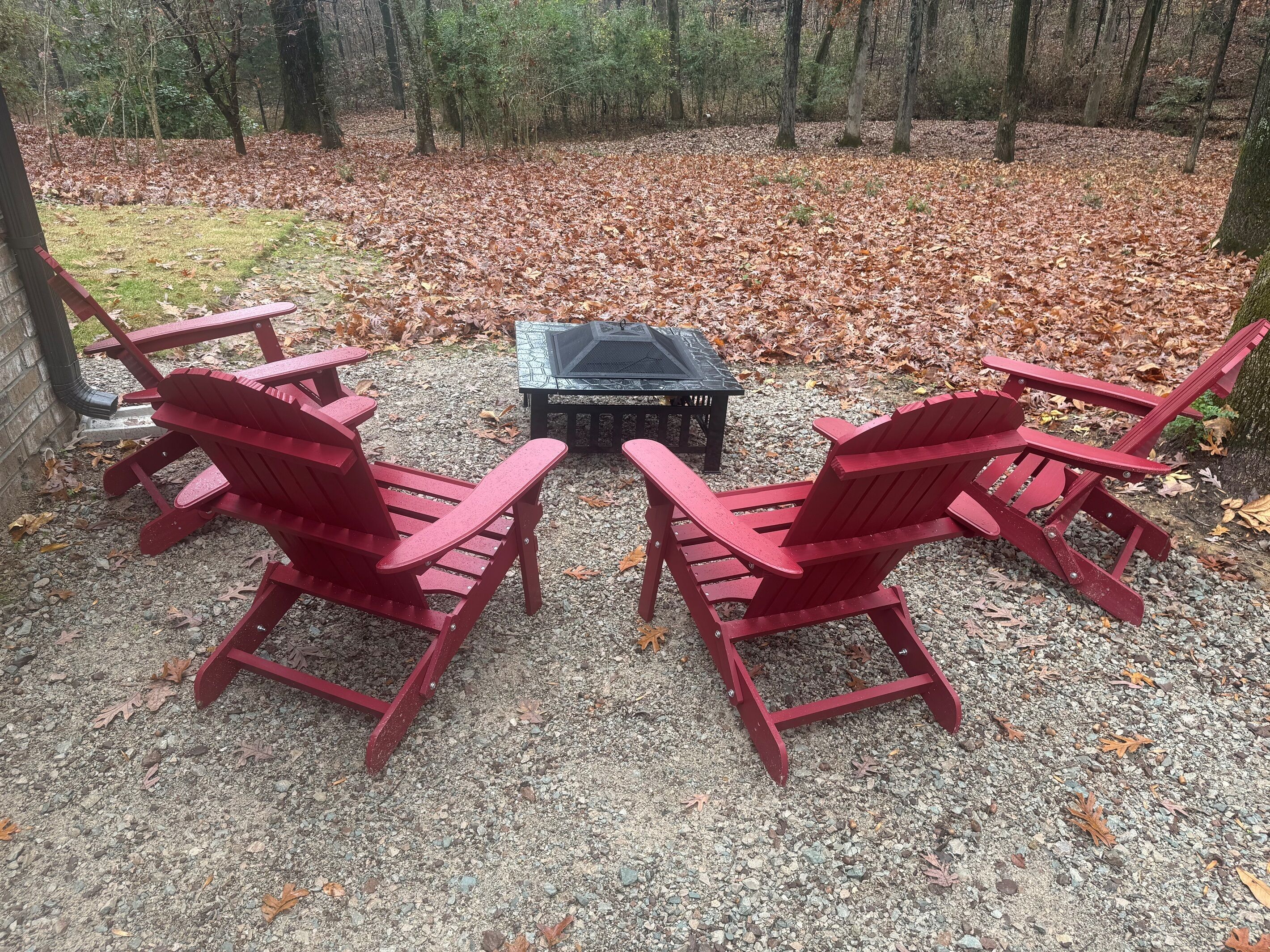 A seating area with red Adirondack chairs and a table, surrounded by a forest.