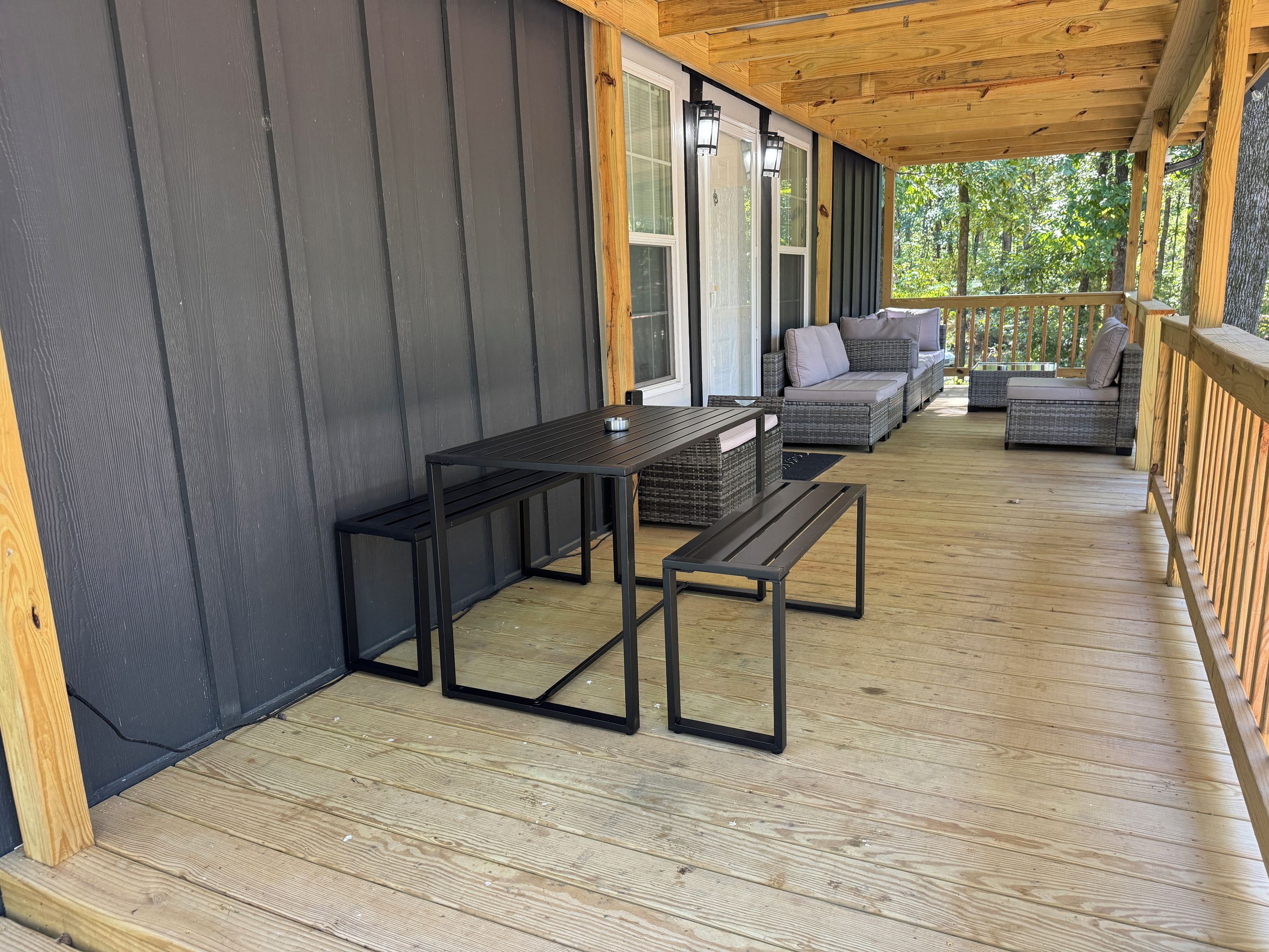 Large covered porch with sectional sofa, coffee table, and dining set, perfect for relaxing in the woods