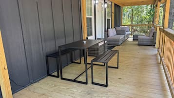 Large covered porch with sectional sofa, coffee table, and dining set, perfect for relaxing in the woods
