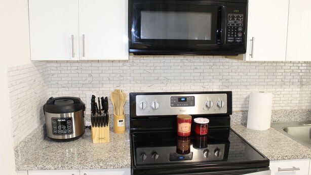 A kitchen with white cabinets, a black microwave, a stainless steel stove, and a countertop with a coffee maker, knives, and jars. - Villa Marita B&B in Middleburg (Middleburg)