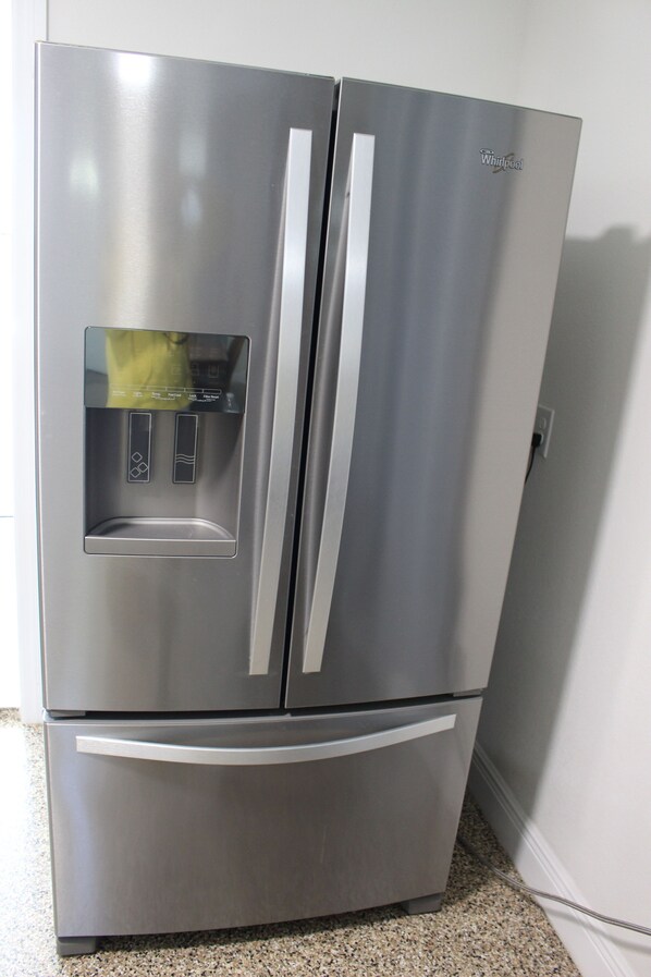 Un refrigerador Whirlpool de acero inoxidable con dispensador de agua y hielo, situado en una cocina con encimeras de granito.