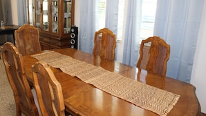 A dining table with a woven placemat, surrounded by wooden chairs with woven backs. A wooden cabinet with glass doors is visible in the background. - Villa Marita B&B in Middleburg (Middleburg)