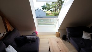 A modern living room with a skylight, dark sofas, a wooden coffee table, and a view of a residential area.