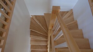 A wooden spiral staircase with a handrail, leading upwards.