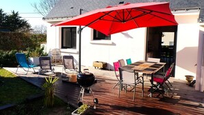 An outdoor patio with a wooden deck, a red umbrella, and a barbecue grill.
