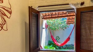 A window with wooden shutters, a red hammock, and green plants. - Pousada Atlantis (Jijoca de Jericoacoara)