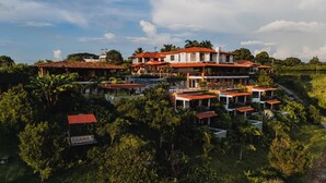 A large, multi-story resort with a swimming pool, surrounded by lush greenery and palm trees.