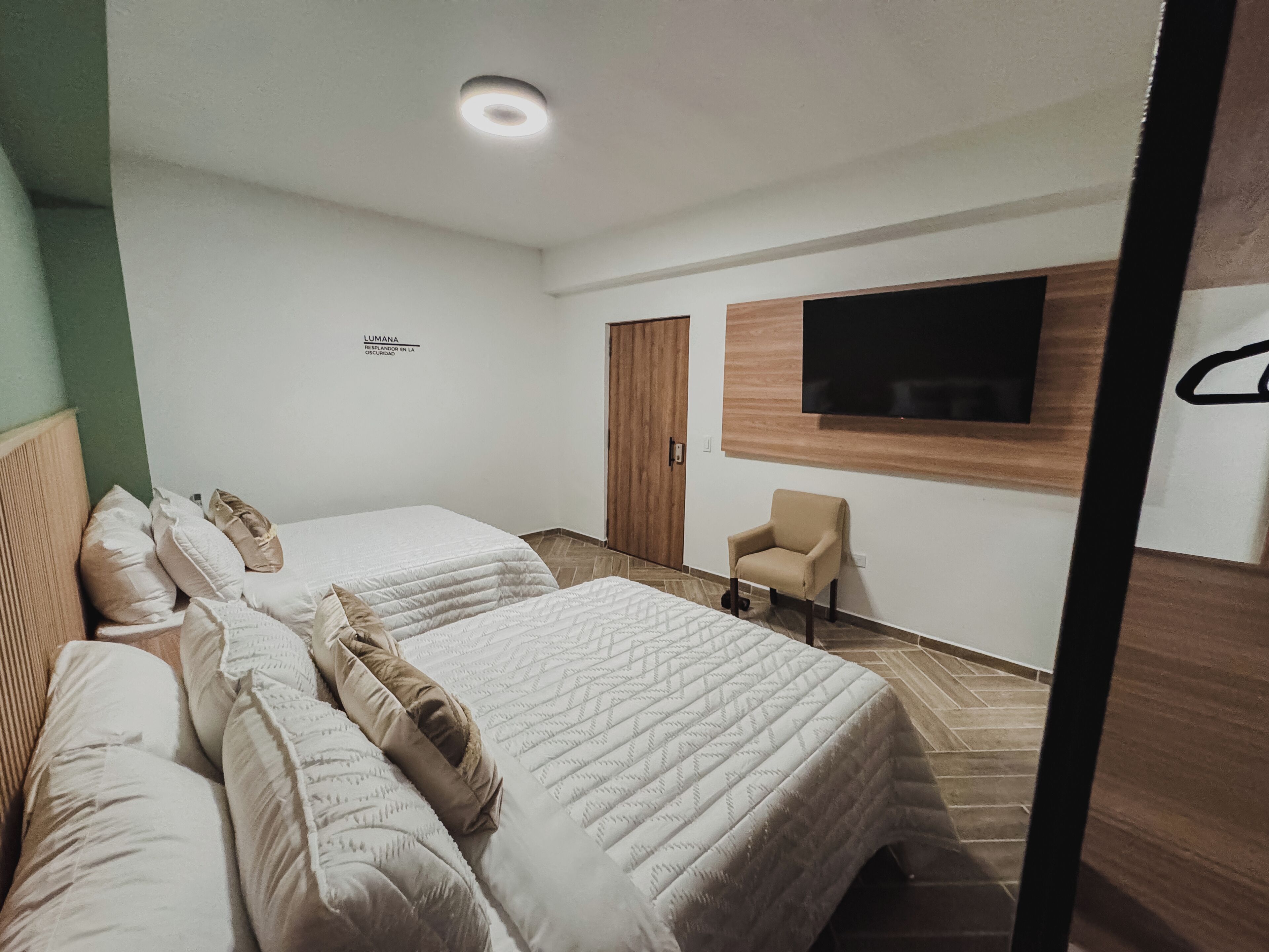 Een hotelkamer met twee bedden, een aan de muur bevestigde televisie, een stoel en een houten garderobe.