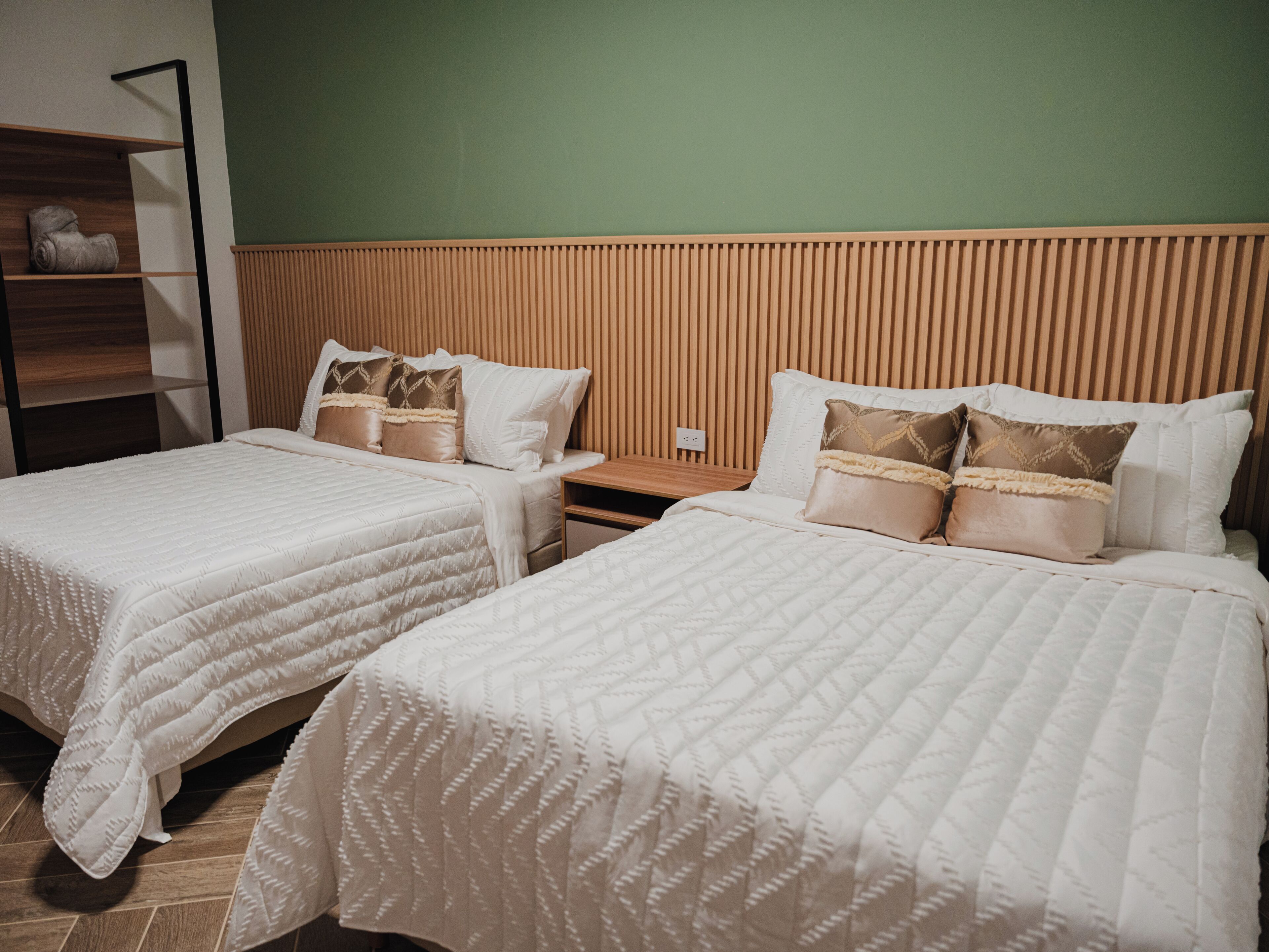 Une chambre d’hôtel avec deux lits, une tête de lit en bois et une table de chevet.