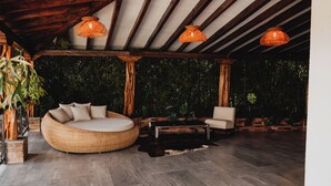 A spacious outdoor seating area with a round wicker sofa and a chair, a wooden table, and hanging wicker lamps.
