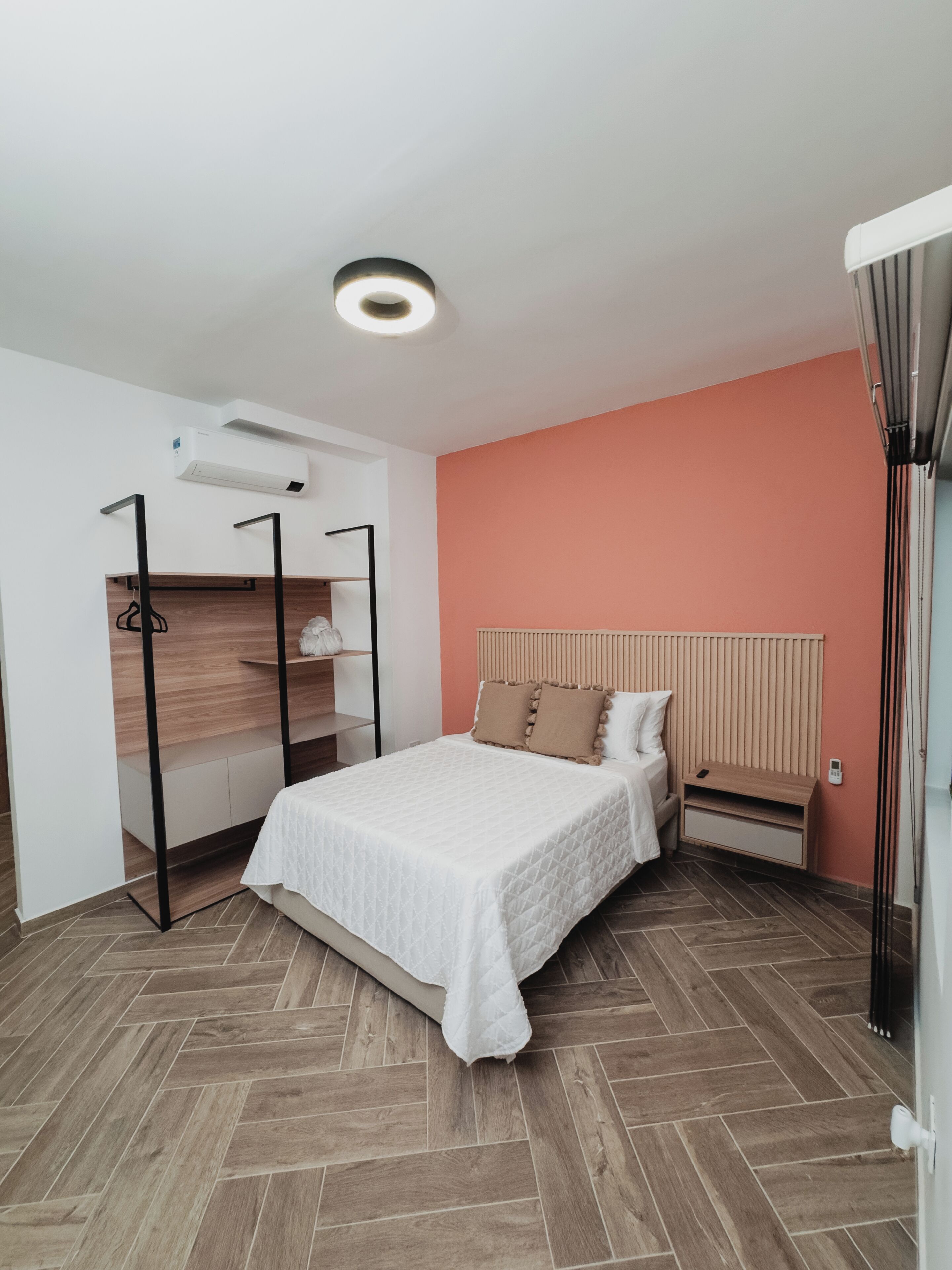 A bedroom with a bed, a wardrobe, a bedside table, and an air conditioning unit.