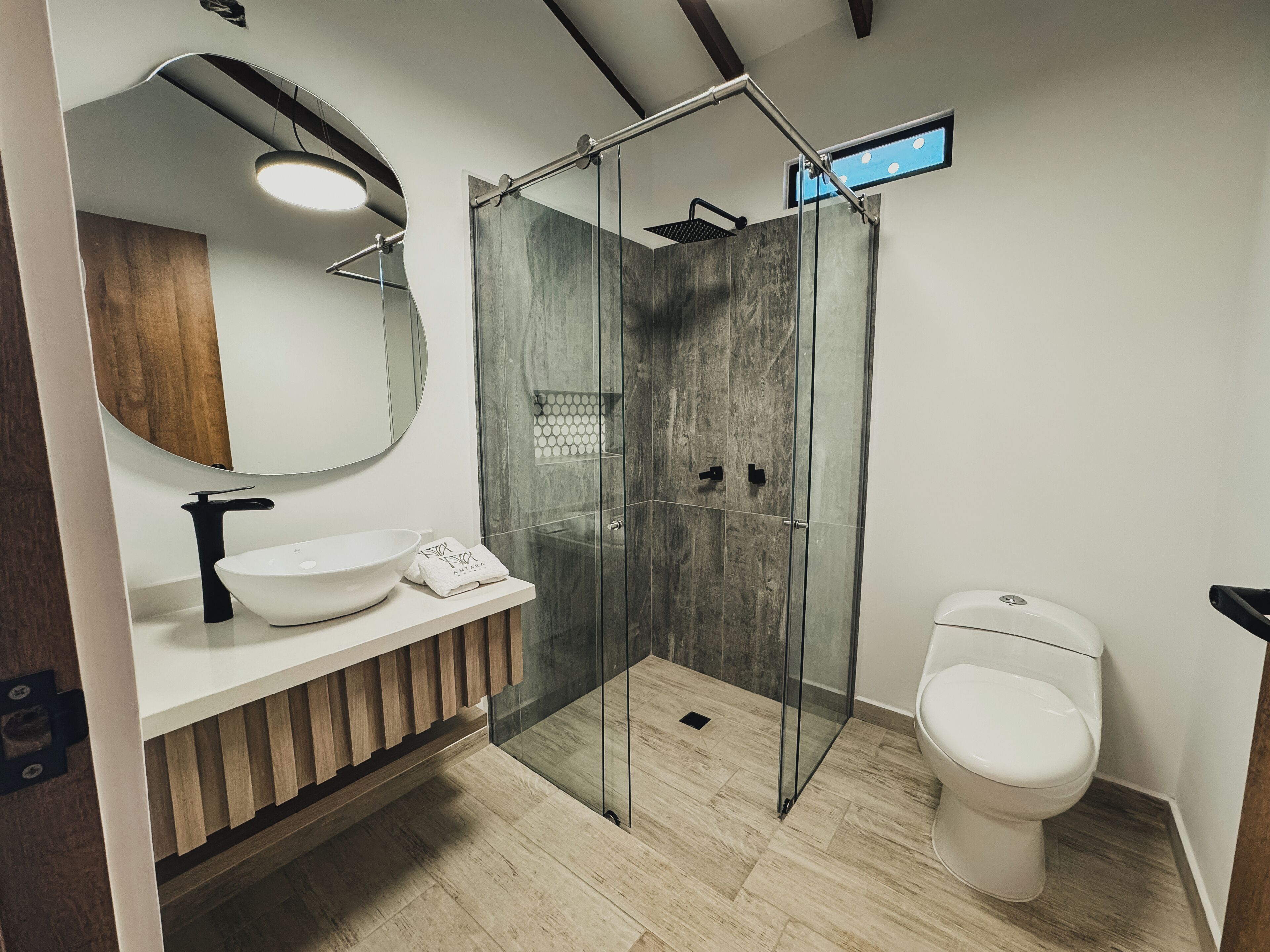 Un baño moderno con ducha envuelta en vidrio, un lavamanos blanco y un inodoro.
