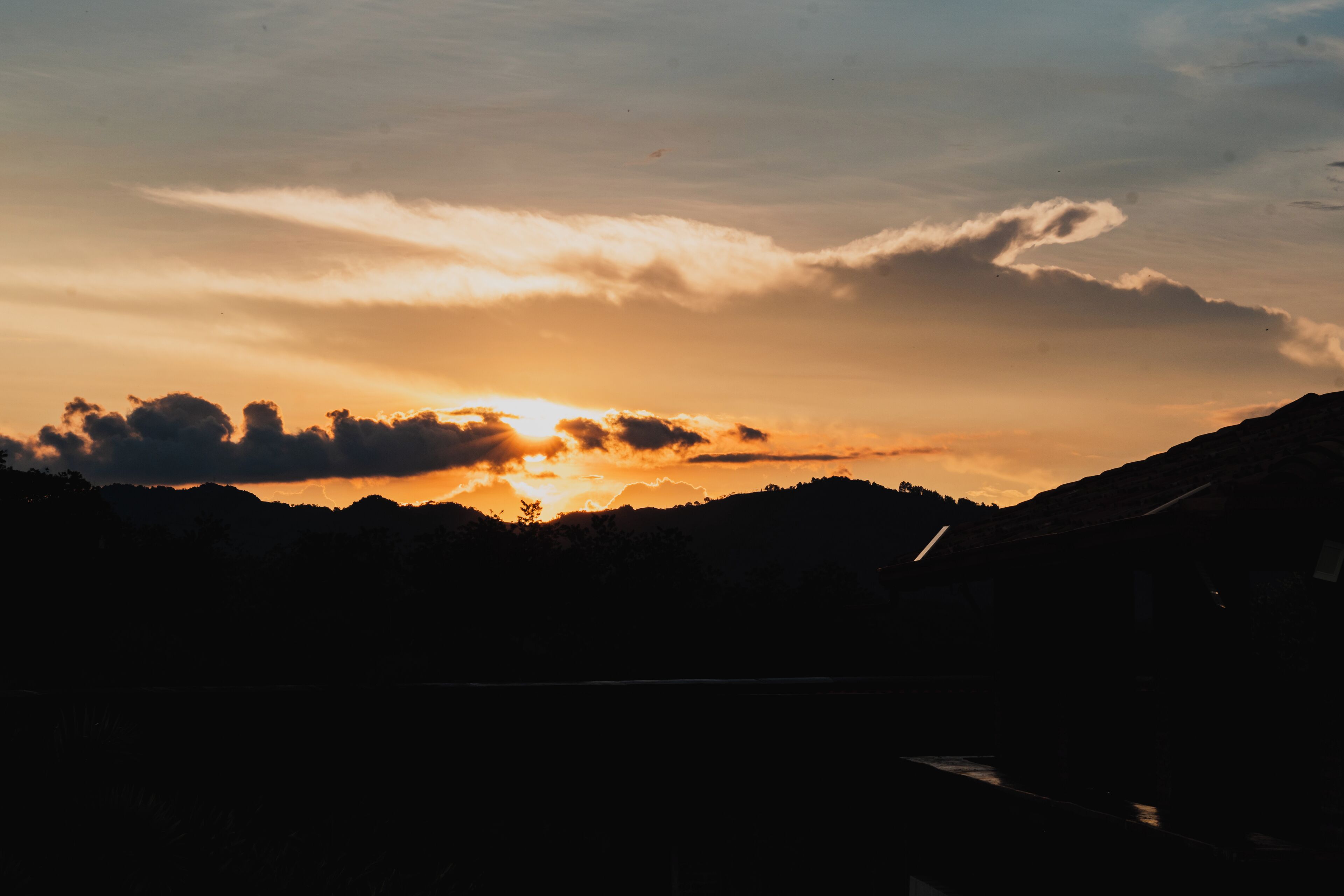 Un coucher de soleil sur un paysage montagneux, avec les silhouettes d’arbres et d’une rivière.