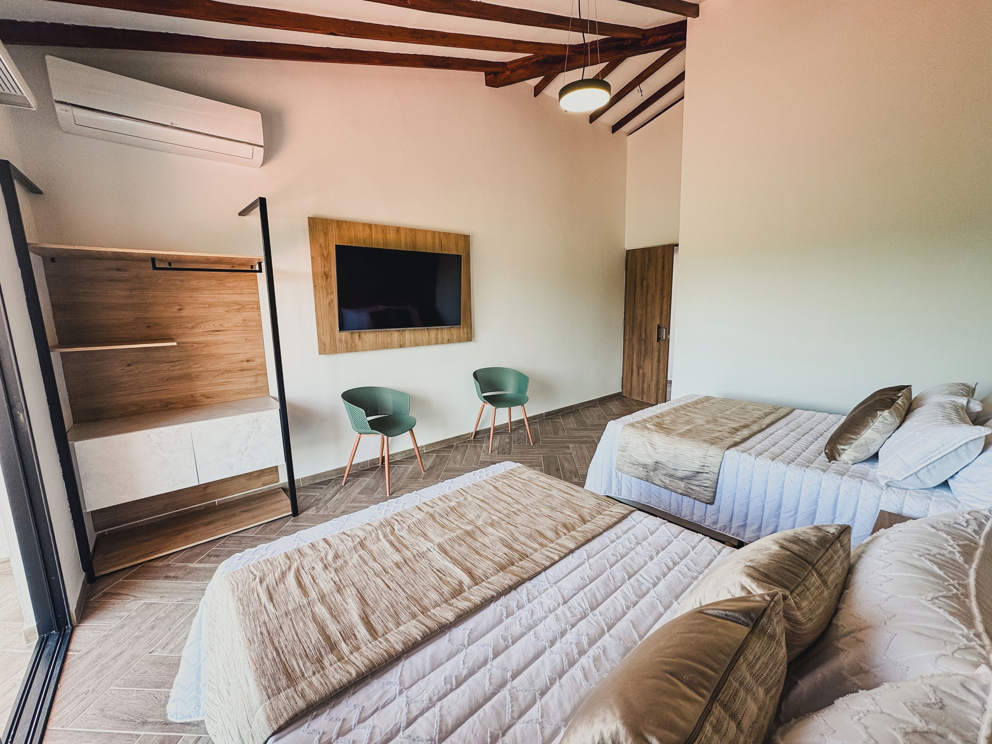 Ein Hotelzimmer mit zwei Betten, einem an der Wand montierten Fernseher und einer Sitzecke mit Stühlen.