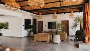 A spacious lobby with wicker furniture, large potted plants, and a high ceiling with woven light fixtures.