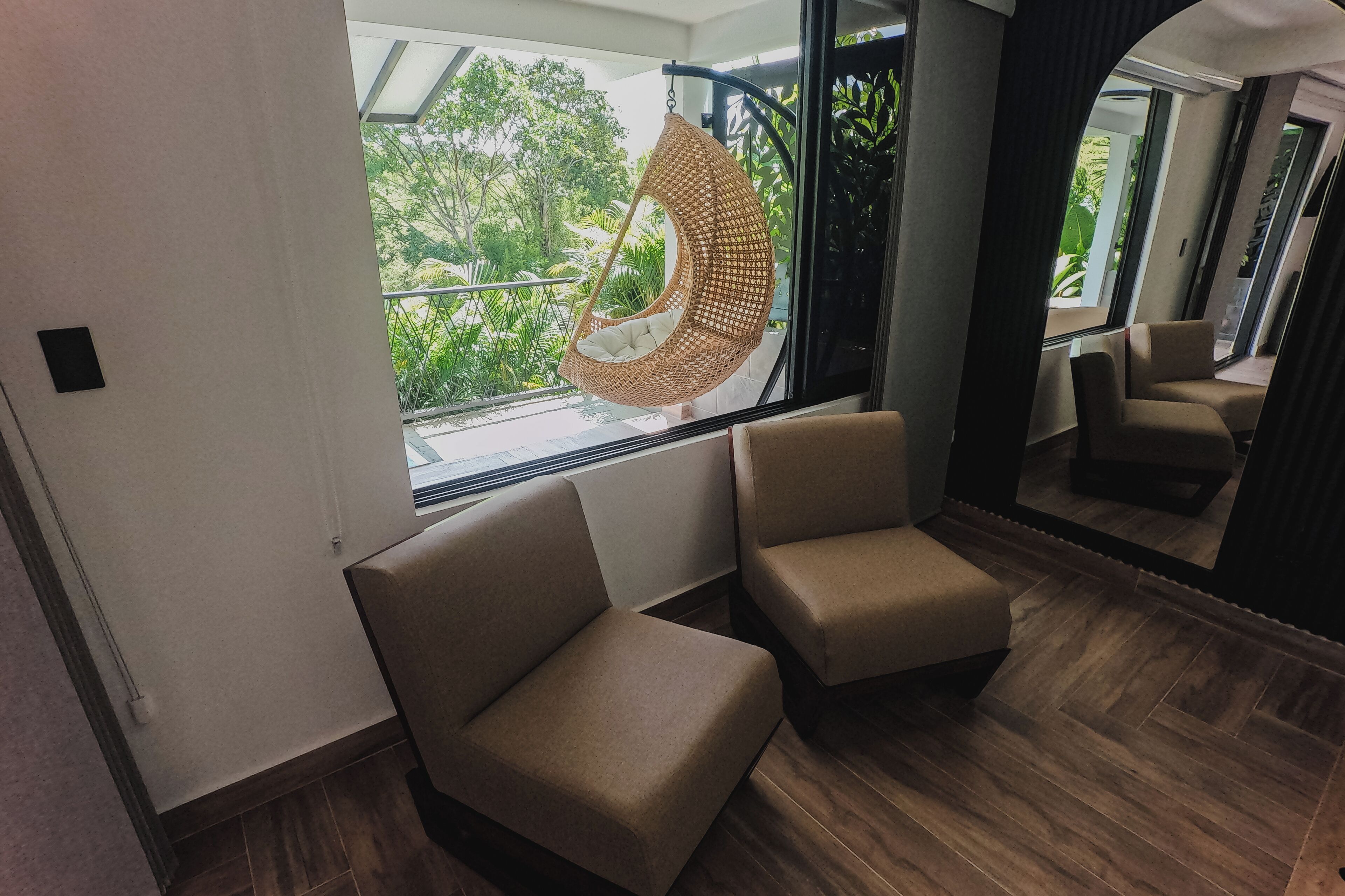 A modern room with a hanging chair, two cushioned chairs, and a large window with a view of greenery.