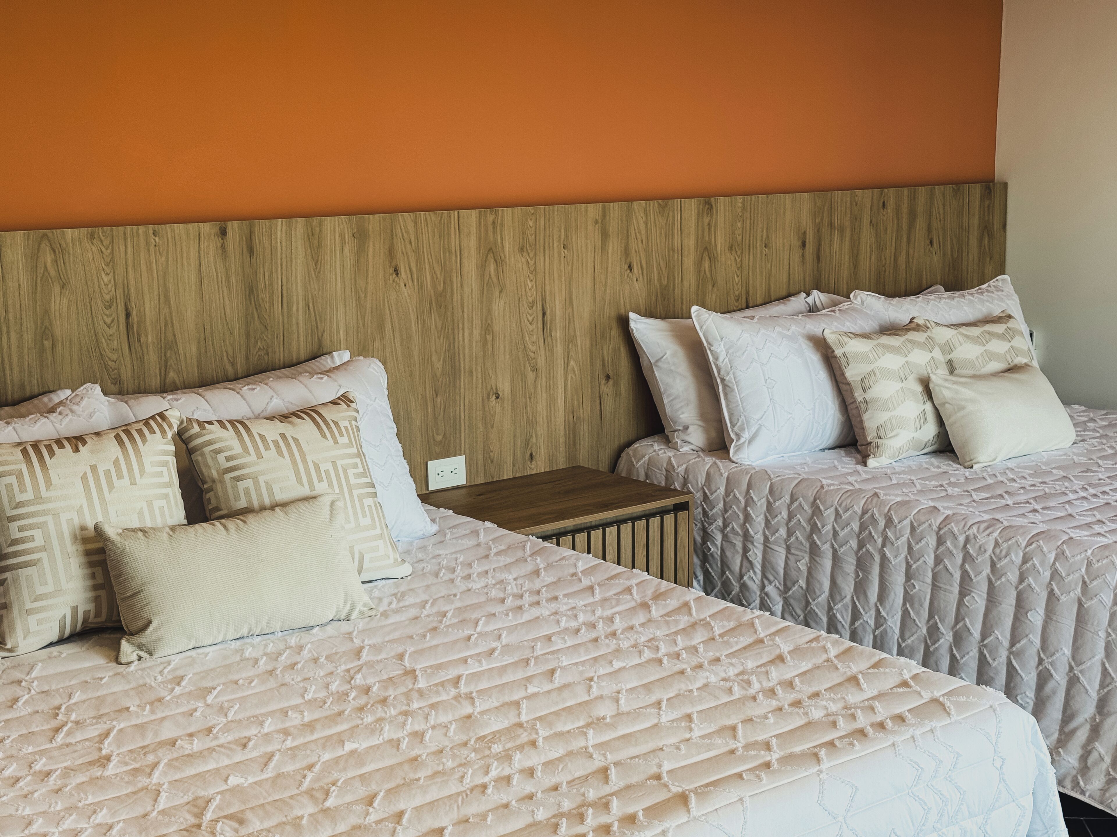 Two beds with patterned bedding, a wooden headboard, and a small bedside table.