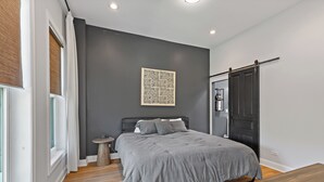 Un dormitorio moderno con cama, mesita de noche, una obra de arte en la pared y una puerta corrediza.