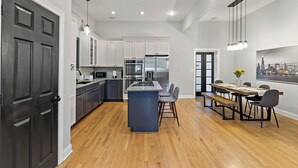 Una cocina moderna con armarios blancos, electrodomésticos de acero inoxidable y un comedor de madera con vistas a la ciudad.
