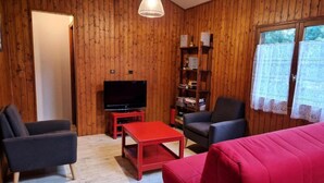 Ein gemütliches Wohnzimmer mit Holzwänden, einem Flachbildfernseher auf einem roten Podest, einem Bücherregal und einem roten Sofa.