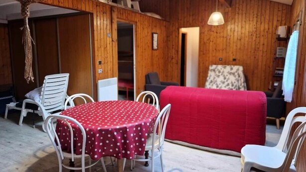 Ein gemütliches Zimmer mit Holzvertäfelung, einem runden Tisch mit einem Tischlein in Punkteoptik und weißen Stühlen.