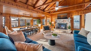 Acogedor interior de cabaña de troncos con comedor, chimenea y sala de estar amoblada con sofás y una mesa de centro.