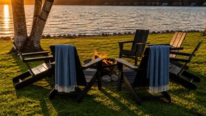Un área de estar al aire libre junto al lago, con sillas y una chimenea.