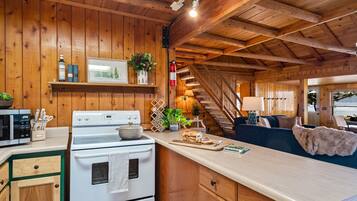 Una cocina acogedora de estilo rústico con paredes de madera, una estufa blanca y un comedor con sofá y mesa.