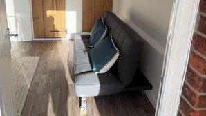 Une pièce avec un canapé gris, un plancher en bois et une porte en bois dotée d’une poignée noire.
