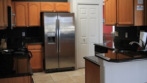 A kitchen with wooden cabinets, a stainless steel refrigerator, a black countertop, and a white door. - Dog Friendly:  Pleasant 4-bedroom pool and spa house near Disney with pool table (Kissimmee)