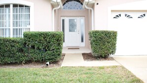 A house with a white front door, a garage with decorative garage doors, and a small front yard with two hedges. - Dog Friendly:  Pleasant 4-bedroom pool and spa house near Disney with pool table (Kissimmee)