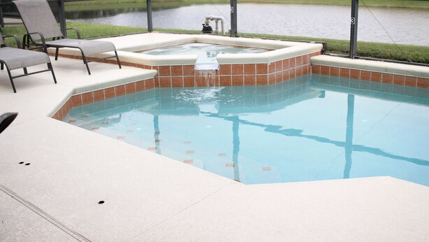 A swimming pool with a hot tub, surrounded by a patio with chairs, and a view of a lake. - Dog Friendly:  Pleasant 4-bedroom pool and spa house near Disney with pool table (Kissimmee)