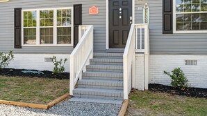 A single-story house with a dark front door, a 'No Entry' sign, and a 'Welcome' sign. There are steps leading to the door, and a small garden area with gravel and plants. - Coastal 3BR w/Game Room, 5 mins to beach, FirePit (Shallotte)